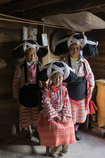 Gaoxing China 29 April 2026 View of Long Horn Miao women wearing traditional elaborate headpieces and colorful embroidered clothing inside a rustic wooden house. Gaoxing China 29 April 2026 View of Long Horn Miao women wearing traditional elaborate headpieces and colorful embroidered clothing inside a rustic wooden house.