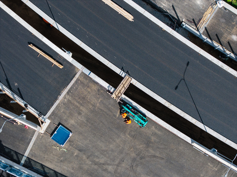 Aerial view of a new road construction site with workers in orange high visibility vests and heavy machinery on the asphalt surface in Riga Latvia. Aerial view of a new road construction site with workers in orange high visibility vests and heavy machinery on the asphalt surface in Riga Latvia.