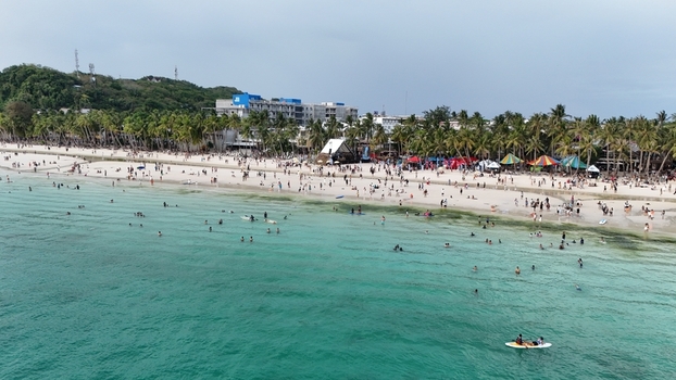 Malay Philippines 02 May 2026 Aerial view of Boracay Island with tourists swimming in turquoise waters and relaxing on the white sand beach lined with palm trees and resorts.