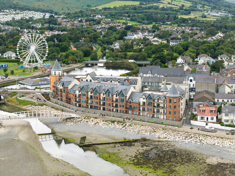Aerial view of Newcastle featuring the Ferris wheel residential buildings a pedestrian bridge over the estuary and green hills Newcastle Northern Ireland United Kingdom. Aerial view of Newcastle featuring the Ferris wheel residential buildings a pedestrian bridge over the estuary and green hills Newcastle Northern Ireland United Kingdom.