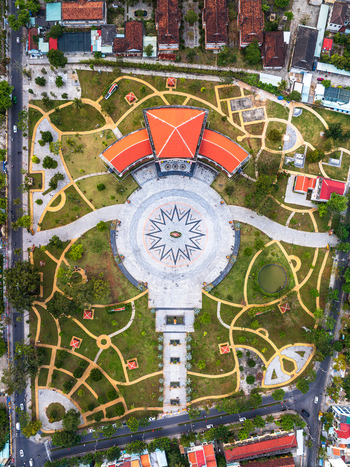 Aerial view of a public plaza featuring a large star shaped mosaic in the center surrounded by manicured green lawns winding pathways and a building with a vibrant red roof in Vietnam. Aerial view of a public plaza featuring a large star shaped mosaic in the center surrounded by manicured green lawns winding pathways and a building with a vibrant red roof in Vietnam.
