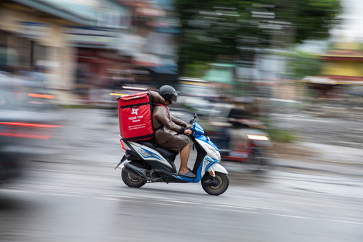 Pokhara Nepal 31 July 2026 View of a delivery driver riding a scooter with a large red thermal box on the back through the streets of the city with motion blur.