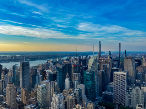 View of the dense Manhattan skyline featuring towering skyscrapers glass facades and the Hudson River under a bright blue sky at sunset in New York New York United States. View of the dense Manhattan skyline featuring towering skyscrapers glass facades and the Hudson River under a bright blue sky at sunset in New York New York United States.