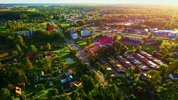 Aerial view of a residential area in a small town surrounded by lush greenery and trees during golden hour in Latvia. Aerial view of a residential area in a small town surrounded by lush greenery and trees during golden hour in Latvia.