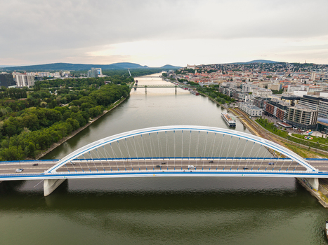 Aerial view of the Apollo Bridge spanning the Danube River with the city skyline and Bratislava Castle in the distance under a cloudy sky in Bratislava Bratislava Region Slovakia. Aerial view of the Apollo Bridge spanning the Danube River with the city skyline and Bratislava Castle in the distance under a cloudy sky in Bratislava Bratislava Region Slovakia.