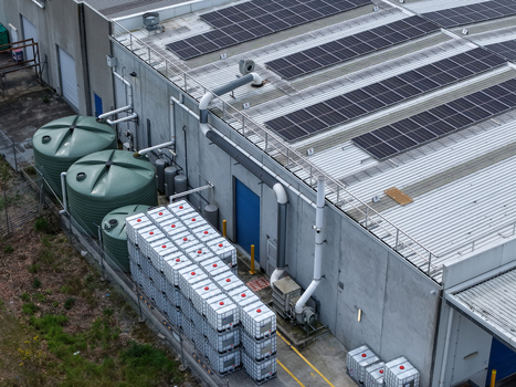 Aerial view of an industrial facility featuring solar panels on the roof large green water storage tanks and stacks of industrial containers in Melbourne VIC Australia.