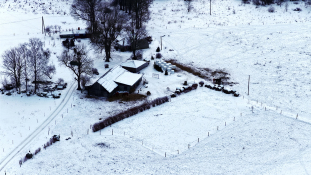 Aerial view of a snow covered rural farmstead with wooden buildings bare trees and fenced pastures in the countryside of Latvia. Aerial view of a snow covered rural farmstead with wooden buildings bare trees and fenced pastures in the countryside of Latvia.