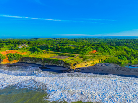 Aerial view of Pantai Pangumbahan Sukabumi featuring a unique black sand beach rugged cliffs and dense tropical forest in Kecamatan Ciracap Jawa Barat Indonesia.