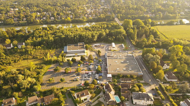 Aerial view of a commercial complex with parking lots surrounded by lush green trees and residential houses near the Seine river in Chartrettes Ile de France France. Aerial view of a commercial complex with parking lots surrounded by lush green trees and residential houses near the Seine river in Chartrettes Ile de France France.