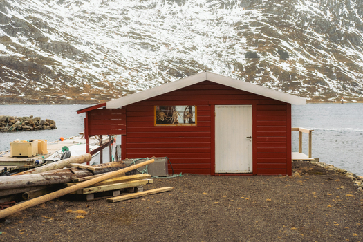 View of a rustic red cabin standing proudly against the backdrop of snow dusted mountains and serene waters Skjelfjorden Nordland Norway. View of a rustic red cabin standing proudly against the backdrop of snow dusted mountains and serene waters Skjelfjorden Nordland Norway.