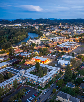 Aerial view of the city of Eugene at dusk featuring the Willamette River residential buildings commercial structures and illuminated streets in Eugene Oregon United States. Aerial view of the city of Eugene at dusk featuring the Willamette River residential buildings commercial structures and illuminated streets in Eugene Oregon United States.