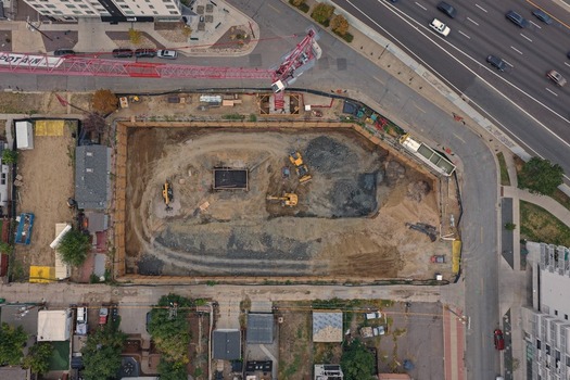 Aerial view of an urban construction site with a large excavated pit a red tower crane and yellow excavators surrounded by city streets in Denver Colorado United States. Aerial view of an urban construction site with a large excavated pit a red tower crane and yellow excavators surrounded by city streets in Denver Colorado United States.