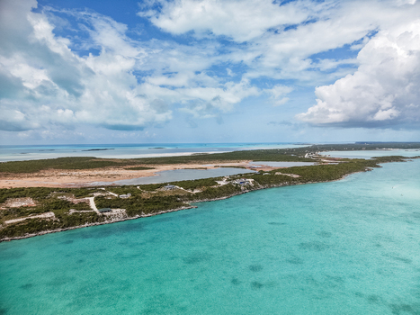 Aerial view of the coastline near Man O War Cay Sandbar with turquoise waters lush vegetation and scattered houses under a cloudy sky Rolletown Exuma The Bahamas. Aerial view of the coastline near Man O War Cay Sandbar with turquoise waters lush vegetation and scattered houses under a cloudy sky Rolletown Exuma The Bahamas.