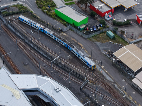Melbourne VIC Australia 25 September 2026 Aerial view of a commuter train at a station platform beside industrial buildings a green warehouse and a gas station.