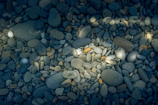 View of smooth rounded beach pebbles and stones illuminated by dappled sunlight at Olympic National Park in Port Angeles Washington United States.