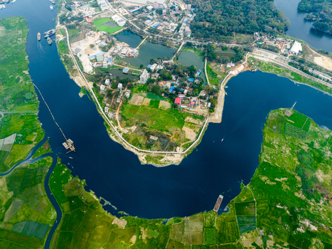 Aerial view of a winding river bend surrounded by lush green agricultural fields small residential clusters and trees in Dhaka Dhaka Division Bangladesh. Aerial view of a winding river bend surrounded by lush green agricultural fields small residential clusters and trees in Dhaka Dhaka Division Bangladesh.