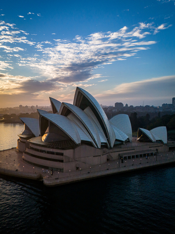 Aerial view of the iconic Sydney Opera House gleams against the fading sunset casting long shadows over the tranquil harbor waters Sydney New South Wales Australia. Aerial view of the iconic Sydney Opera House gleams against the fading sunset casting long shadows over the tranquil harbor waters Sydney New South Wales Australia.