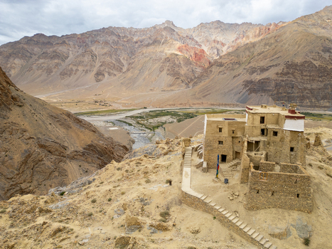 Aerial view of an ancient stone monastery perched on a rocky cliff overlooking the Zanskar valley with rugged mountains and a winding river in Zanskar Ladakh India.