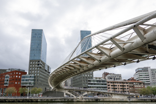 View of the Zubizuri bridge and Isozaki Atea towers with modern architecture and a cloudy sky in Greater Bilbao Basque Country Spain. View of the Zubizuri bridge and Isozaki Atea towers with modern architecture and a cloudy sky in Greater Bilbao Basque Country Spain.