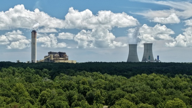 Aerial view of the Seminole Generating Station with cooling towers and smokestack rising above dense forest under a blue sky in Palatka Florida United States.
