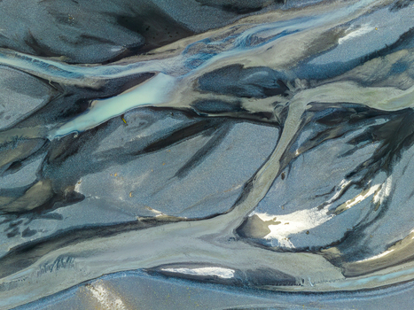Aerial view of braided glacial river channels with dark volcanic sand and light blue meltwater flowing through the landscape of Iceland. Aerial view of braided glacial river channels with dark volcanic sand and light blue meltwater flowing through the landscape of Iceland.