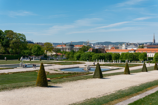 View of the manicured gardens of Belvedere Palace with fountains and cone shaped hedges under a clear blue sky in Vienna Austria. View of the manicured gardens of Belvedere Palace with fountains and cone shaped hedges under a clear blue sky in Vienna Austria.