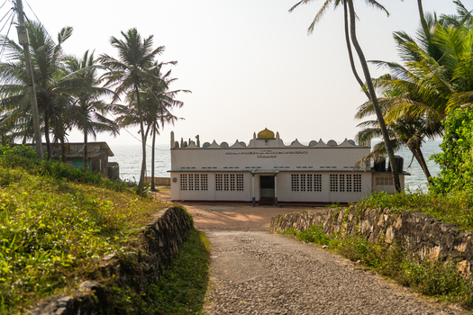 View of a white mosque with a golden dome on the coast framed by tall palm trees and a stone path in Galle Southern Province Sri Lanka.