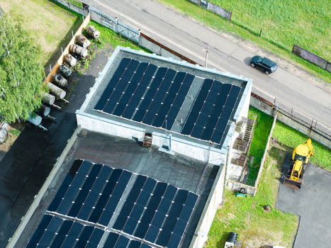 Aerial view of solar panels installed on a flat industrial building roof with a yellow backhoe loader parked nearby and storage tanks in Olaine Olaine Municipality Latvia. Aerial view of solar panels installed on a flat industrial building roof with a yellow backhoe loader parked nearby and storage tanks in Olaine Olaine Municipality Latvia.