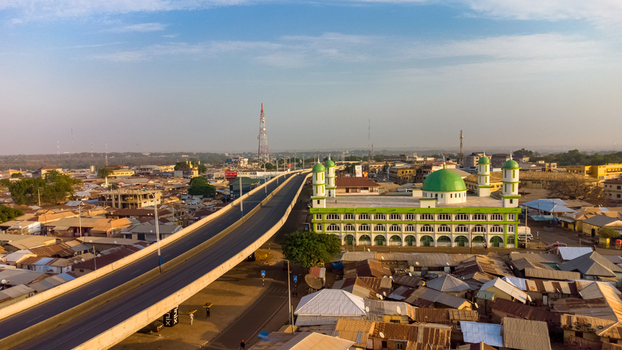 Tamale Northern Region Ghana 16 March 2023 Aerial view of the Tamale Interchange and a nearby mosque with a green dome surrounded by urban rooftops and infrastructure under a clear sky.