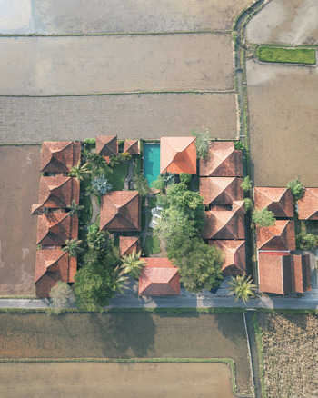 Aerial view of a resort complex with terracotta tiled roofs and a swimming pool nestled within lush green rice paddies in Ubud Bali Indonesia. Aerial view of a resort complex with terracotta tiled roofs and a swimming pool nestled within lush green rice paddies in Ubud Bali Indonesia.