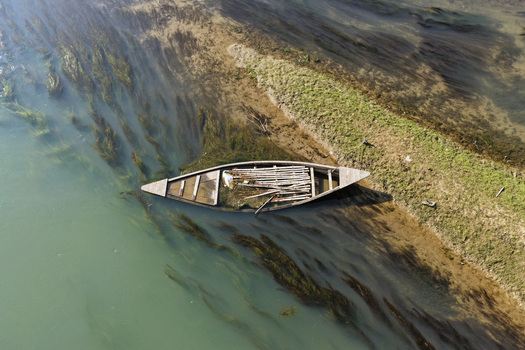 Aerial view of a small wooden boat resting on the grassy riverbank of a calm river with aquatic plants visible in the clear water in Joypurhat Rajshahi Division Bangladesh. Aerial view of a small wooden boat resting on the grassy riverbank of a calm river with aquatic plants visible in the clear water in Joypurhat Rajshahi Division Bangladesh.