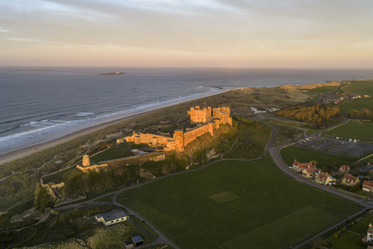 Aerial view of Bamburgh Castle on a rocky outcrop overlooking the sandy beach and North Sea at sunset in Bamburgh England United Kingdom. Aerial view of Bamburgh Castle on a rocky outcrop overlooking the sandy beach and North Sea at sunset in Bamburgh England United Kingdom.