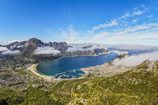 Aerial view of Hout Bay with its harbour sandy beach and surrounding mountains under a clear blue sky in Cape Town Western Cape South Africa.