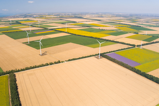 Aerial view of wind turbines standing in vast agricultural fields with patches of yellow crops and green vegetation in Saints Constantine and Helena Varna Bulgaria.