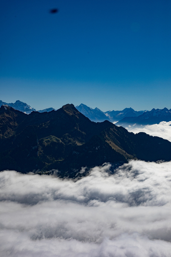 Aerial view of the Swiss Alps with dramatic mountain peaks rising above a thick blanket of clouds under a clear blue sky in Airolo Ticino Switzerland. Aerial view of the Swiss Alps with dramatic mountain peaks rising above a thick blanket of clouds under a clear blue sky in Airolo Ticino Switzerland.