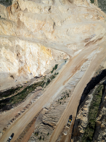Aerial view of a large open pit quarry with terraced rock walls dirt access roads and heavy machinery operating in Teulada Valencian Community Spain.