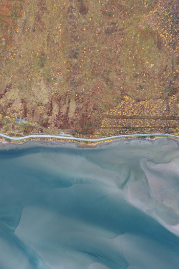 Aerial view of the coastline of Senja featuring a winding road along the shore autumn colored vegetation and clear blue water with sandy tidal flats in Senja Troms Norway.