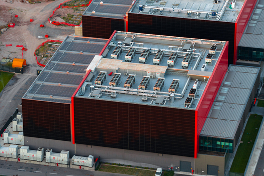 Aerial view of a modern datacenter featuring rooftop HVAC units and a distinctive red and black facade in Settecamini Lazio Italy.
