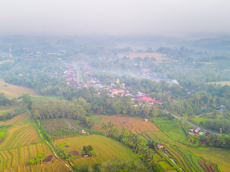 Aerial view of Kemumu village surrounded by lush rice terraces and tropical trees in the misty landscape of Arma Jaya Bengkulu Indonesia. Aerial view of Kemumu village surrounded by lush rice terraces and tropical trees in the misty landscape of Arma Jaya Bengkulu Indonesia.