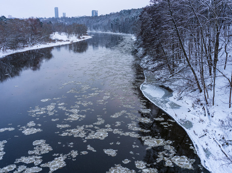 Aerial view of the Neris river flowing through a snowy landscape with ice floes bare trees and the city skyline in the background in Vilnius Vilnius County Lithuania. Aerial view of the Neris river flowing through a snowy landscape with ice floes bare trees and the city skyline in the background in Vilnius Vilnius County Lithuania.