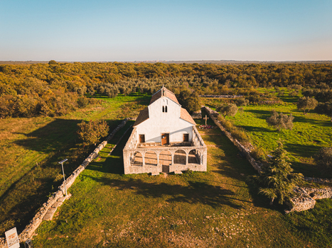 Aerial view of the radiant white church standing proudly amid the verdant landscape framed by ancient stone walls and a dense forest backdrop Vodnjan Istria County Croatia.