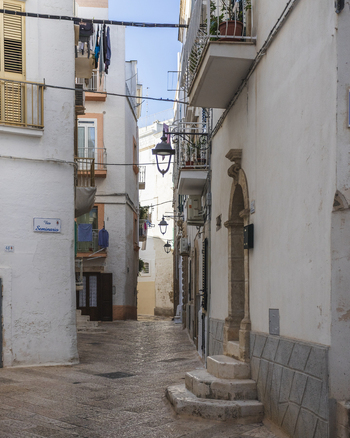 View of a narrow cobblestone alleyway lined with traditional white washed buildings hanging laundry and vintage street lamps in the historic center of Polignano a Mare Apulia Italy.