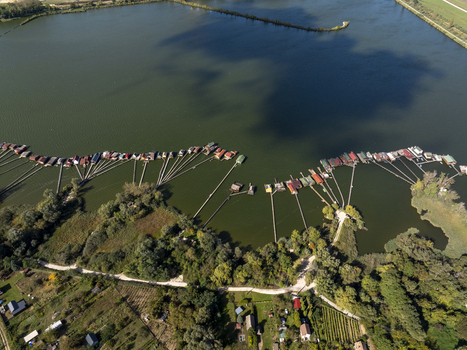 Aerial view of Bokodi Floating Village featuring colorful wooden houses on stilts connected by long piers over the calm lake surrounded by lush greenery in Oroszlany Hungary. Aerial view of Bokodi Floating Village featuring colorful wooden houses on stilts connected by long piers over the calm lake surrounded by lush greenery in Oroszlany Hungary.