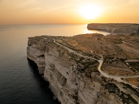 Aerial view of rugged cliffs meet the azure sea under a golden sunset sky at Sanap Cliffs Munxar Gozo Malta. Aerial view of rugged cliffs meet the azure sea under a golden sunset sky at Sanap Cliffs Munxar Gozo Malta.