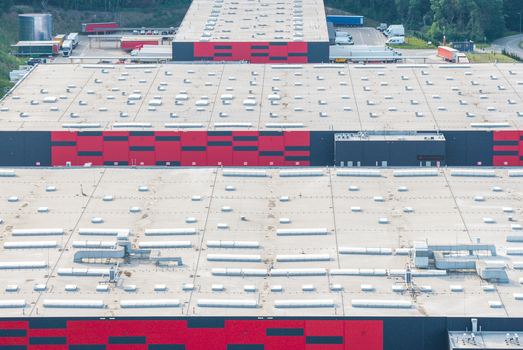 Aerial view of a large logistics center with a flat roof featuring numerous vents and a distinctive red and black facade in Kowale Pomeranian Voivodeship Poland. Aerial view of a large logistics center with a flat roof featuring numerous vents and a distinctive red and black facade in Kowale Pomeranian Voivodeship Poland.
