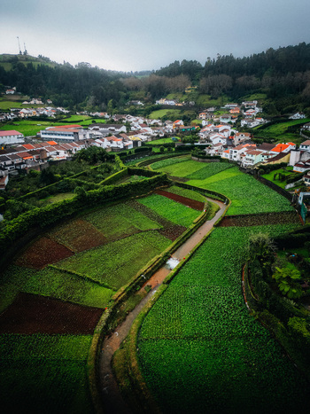 Aerial view of patchwork fields curve through the landscape contrasting with the white buildings nestled in green hills Furnas Azores Portugal.