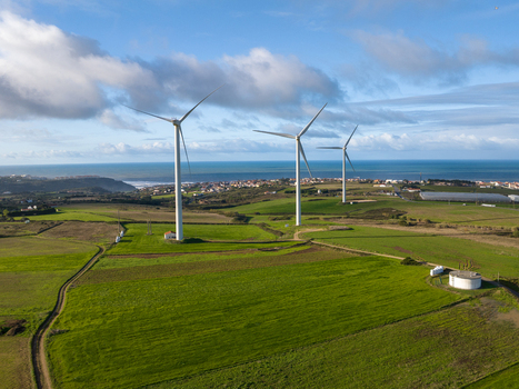 Aerial view of wind turbines standing on lush green fields near the coast under a cloudy sky in Portugal. Aerial view of wind turbines standing on lush green fields near the coast under a cloudy sky in Portugal.