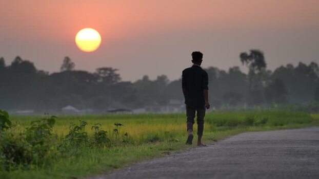 View of a man walking on a rural road at sunset in Bangladesh. View of a man walking on a rural road at sunset in Bangladesh.