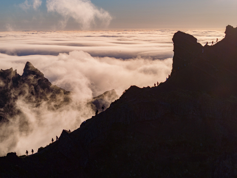 Aerial view of hikers walking along a rugged mountain ridge above a thick layer of clouds at sunset in Madeira. Aerial view of hikers walking along a rugged mountain ridge above a thick layer of clouds at sunset in Madeira.