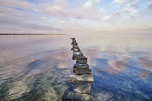 View of the stone path leading into the calm waters of the Saline dello Stagnone at sunset with reflections of the sky in Marsala Sicilia Italy.